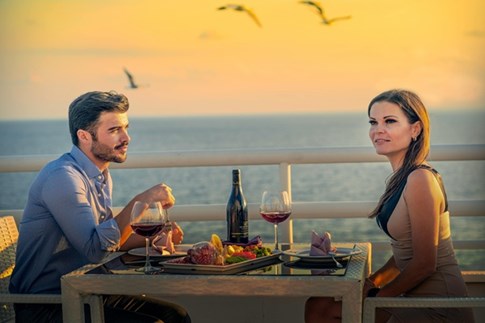 Ein elegant gekleidetes Paar genießt ein Abendessen mit Blick aufs Meer - © Chefmade