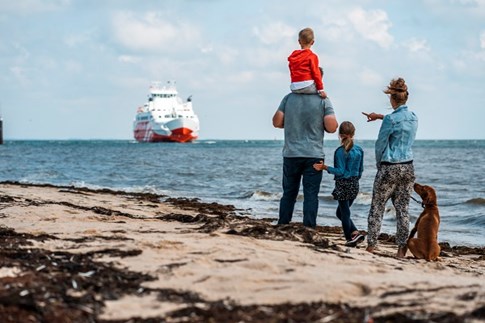 Eine Familie mit Hund beobachtet die FRS Syltfähre vom Strand aus