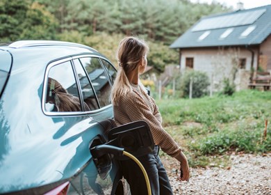 Junge Frau lädt ihr E-Auto vor Ferienhaus in Dänemark